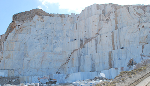Cantera de mármol con grandes bloques de piedra blanca y maquinaria en la base junto a una pendiente de tierra.

Descripción generada con IA