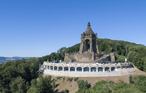 Monumento histórico de piedra ubicado en una colina rodeada de árboles bajo un cielo despejado.

Descripción generada con IA