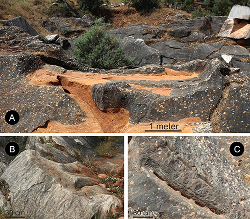 Restos arqueológicos de piedra con inscripciones y marcas talladas en un entorno natural rocoso y seco.

Descripción generada con IA